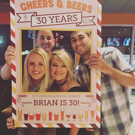 group of party goers posing with Cheers & Beers photo booth frame prop