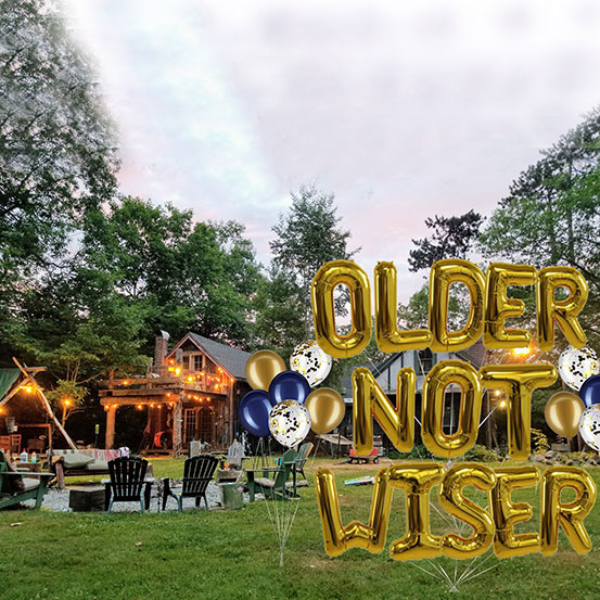 Older Not Wiser spelled out with giant gold letter balloons at an outdoor celebration