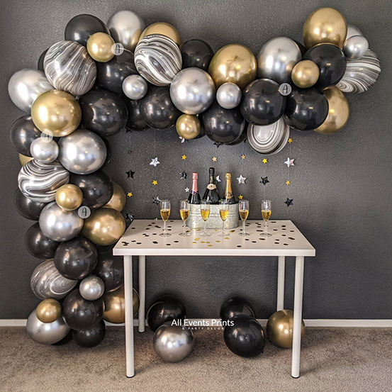 black, gold, and silver balloon garland hung on wall and draped around a party drinks table
