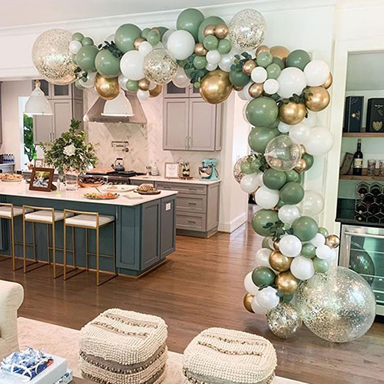 green, white, and gold balloon garland draped around the doorway of an open plan kitchen