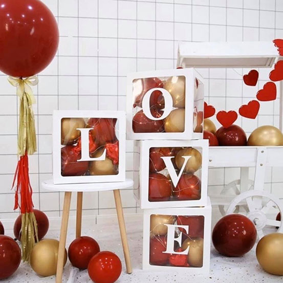 4 transparent boxes filled with red and gold balloons with LOVE spelled out on the sides