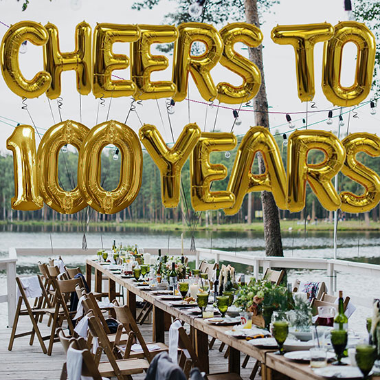 Cheers to 100 years spelled out with giant gold letter balloons above birthday dining tables