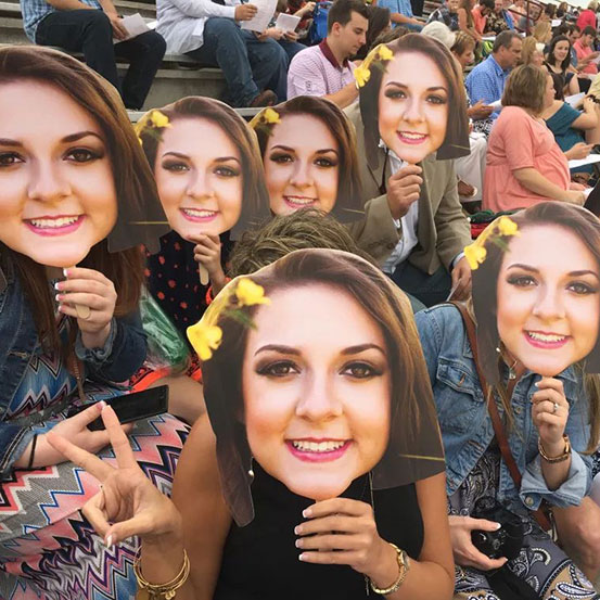 Group of people at a party holding up fan faces of the birthday girl's face