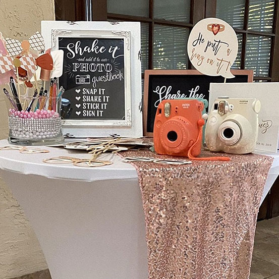 Polaroid guest book on table next to a Polaroid camera and a sign asking guests to Snap It, Shake It, Stick It, Sign It