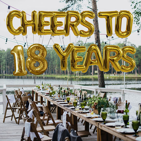 Cheers to 18 years spelled out with giant gold letter balloons above birthday dining tables