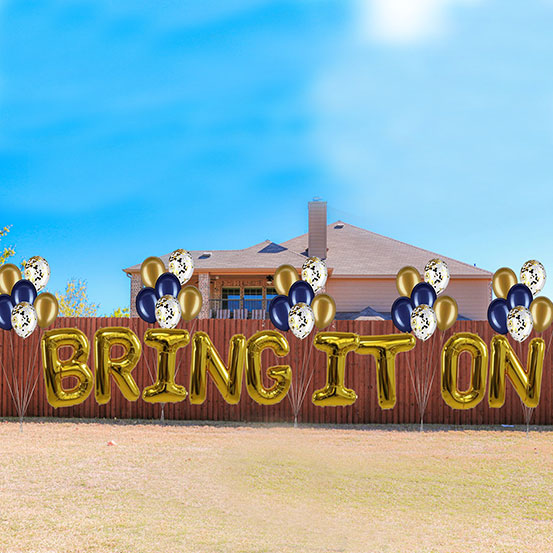 Bring It On spelled out with giant gold letter balloons along a fence in a yard