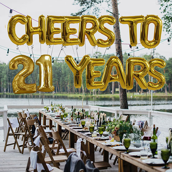 Cheers to 21 years spelled out with giant gold letter balloons above birthday dining tables