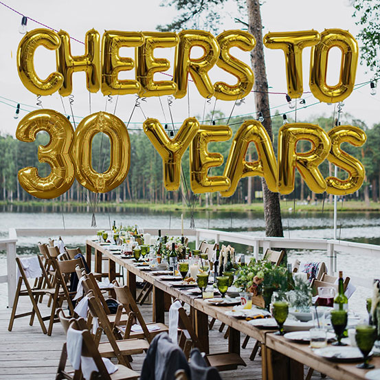 Cheers to 30 years spelled out with giant gold letter balloons above birthday dining tables