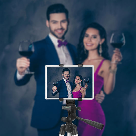 man and woman raising their glasses to toast while recording a video message on a tablet on a tripod