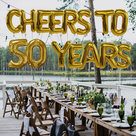 Cheers to 50 years spelled out with giant gold letter balloons above birthday dining tables