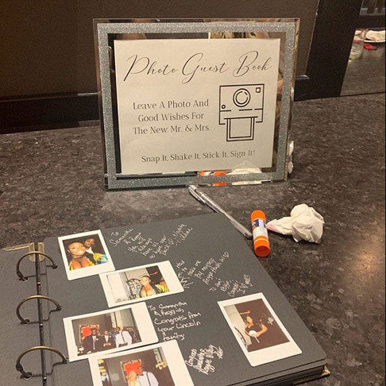 Polaroid guest book on table next to a Polaroid camera and a sign asking guests to Snap It, Shake It, Stick It, Sign It