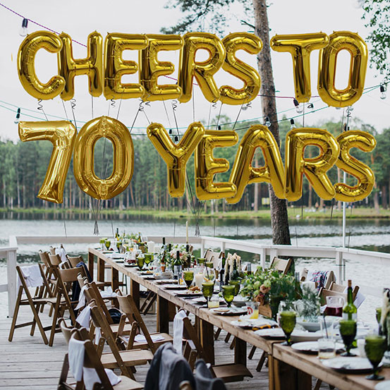 Cheers to 70 years spelled out with giant gold letter balloons above birthday dining tables