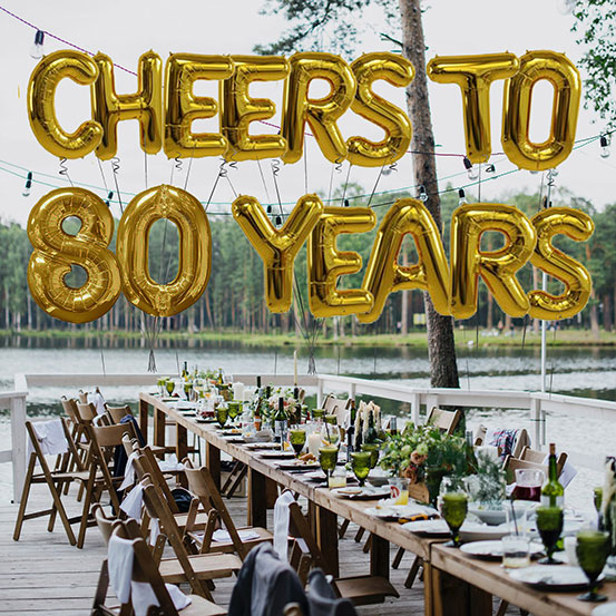Cheers to 80 years spelled out with giant gold letter balloons above birthday dining tables