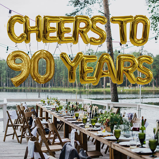 Cheers to 90 years spelled out with giant gold letter balloons above birthday dining tables