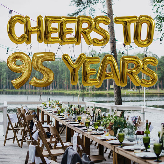 Cheers to 95 years spelled out with giant gold letter balloons above birthday dining tables