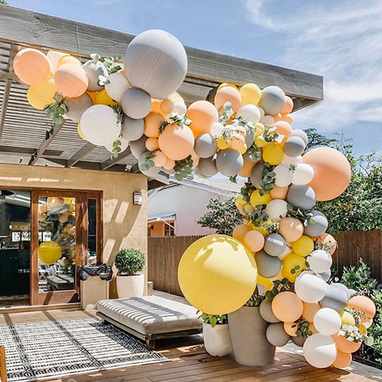 Gray, yellow and peach balloon garland draped around outside seating area of a house