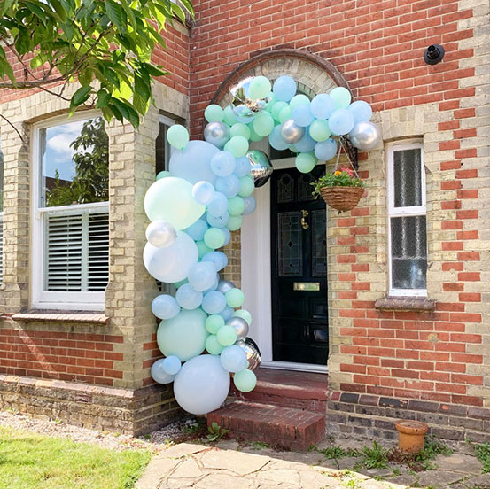 Pale blue and green balloon garland surrounding the entrance to a house