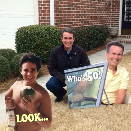 man standing next to half body cut outs of himself at different ages in front yard to celebrate a milestone birthday