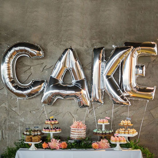 Giant silver letter balloons spelling the word CAKE above a dessert table
