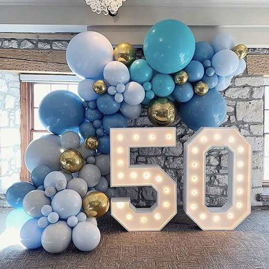 blue, white, and gold balloon garland draped around illuminated 50 number cut outs