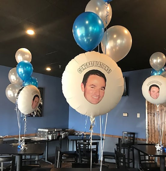 Congratulations helium filled photo balloon with man's face and blue and silver latex balloons used as centerpieces for dining tables
