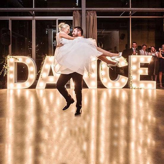 Large marquee letters spelling DANCE with bride & groom on dancefloor
