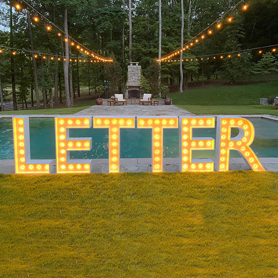 Large marquee letters spelling LETTER on grass next to pool