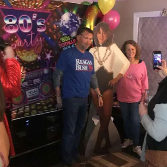 woman standing next to a life size cutout of herself at an 80s theme party