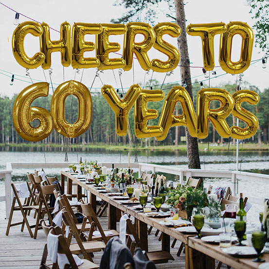 Cheers to 60 years spelled out with giant gold letter balloons above birthday dining tables