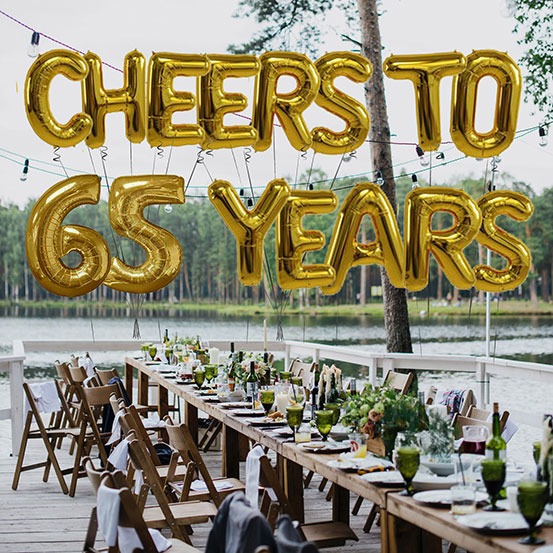 Cheers to 65 years spelled out with giant gold letter balloons above birthday dining tables