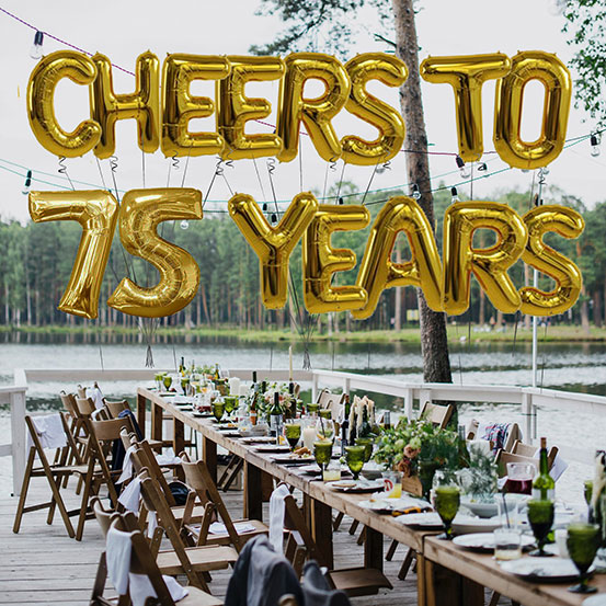 Cheers to 75 years spelled out with giant gold letter balloons above birthday dining tables