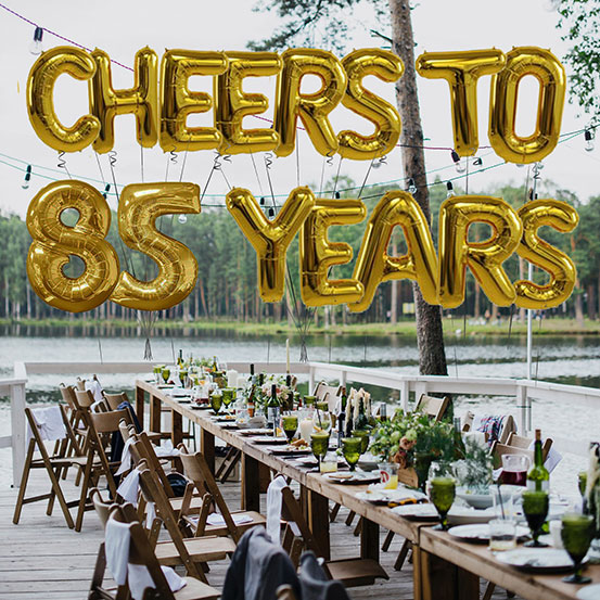 Cheers to 85 years spelled out with giant gold letter balloons above birthday dining tables