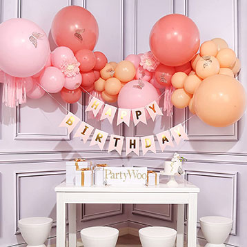 pastel pink and orange balloon garland and birthday banner hung above table