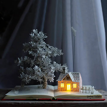 book sculpture of tree and house with light inside